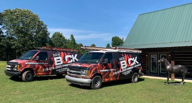 New Buck Chimney Services Trucks in front of a log cabin type house with a green roof and horse statue